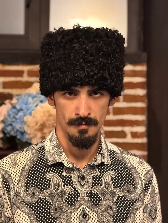 Karakul Papakha: black karakul with short, tight curls, tall straight-sided shape with a flat top, worn, front view