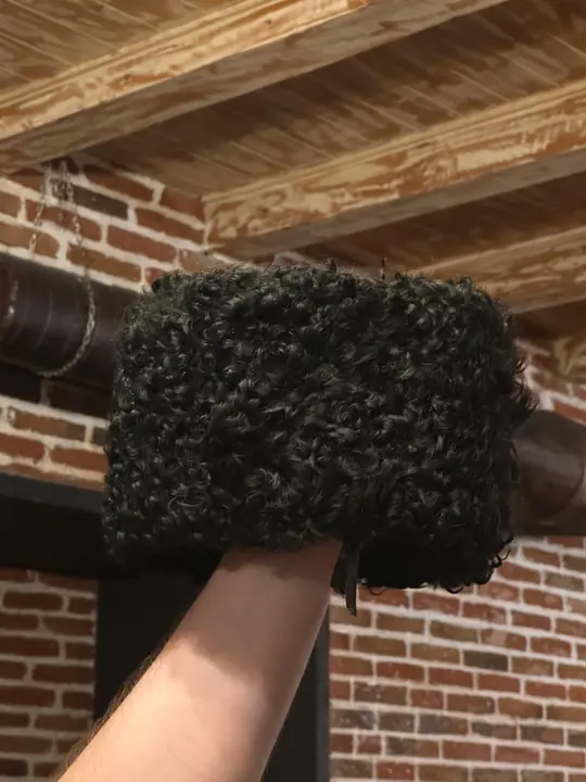 Karakul Papakha held in a hand, side view: the short black curls and straight sides