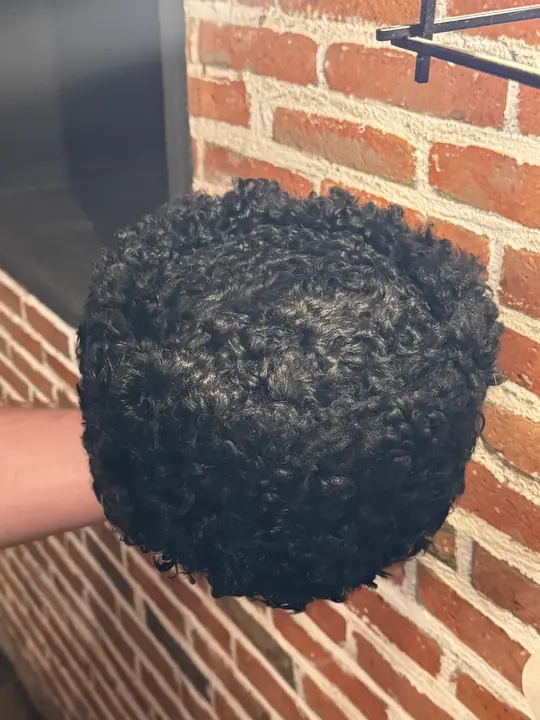 Karakul Papakha held in a hand, seen from above: the flat top covered in tight black curls