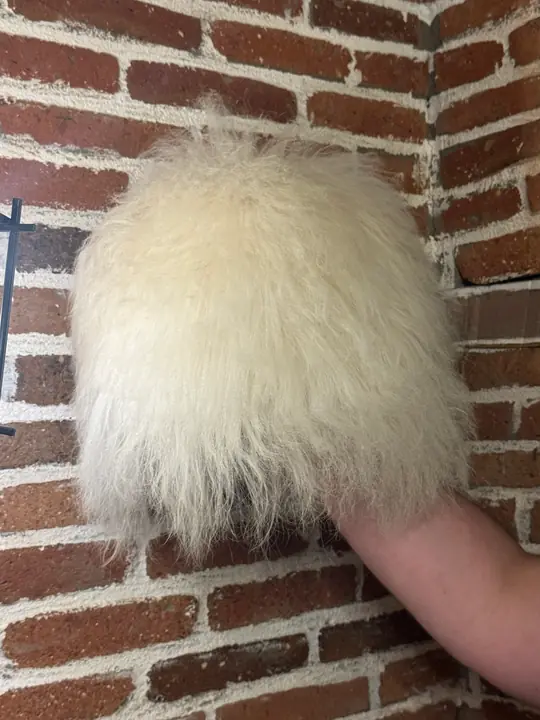 Very White Sheepskin Papakha held in a hand, side view: a tall shape of straight white wool