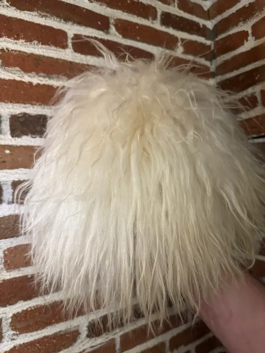 Very White Sheepskin Papakha held in a hand: long straight bright white wool seen from the side