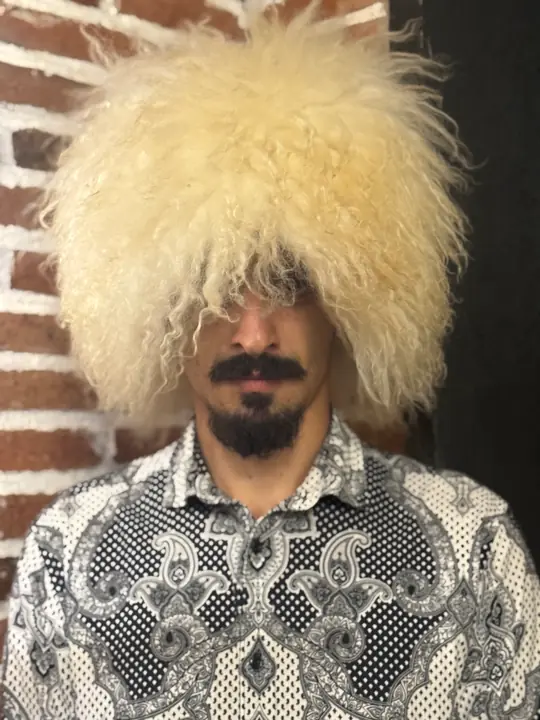 White Sheepskin Papakha: cream-white sheepskin with long wavy wool, full rounded shape, worn, front view with the wool over the eyes