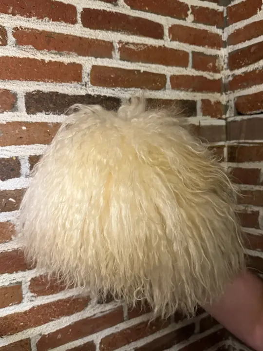 White Sheepskin Papakha held in a hand, seen from the side: the rounded shape and long wavy wool
