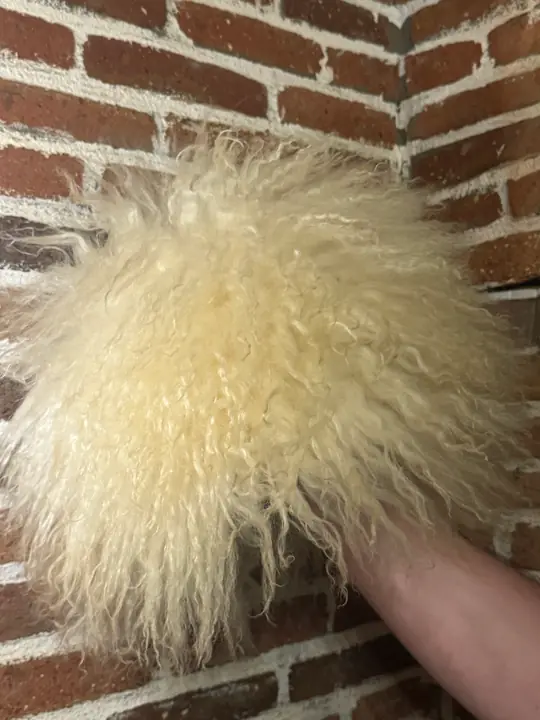 White Sheepskin Papakha held in a hand, seen from above: the long wavy cream-white wool spreads out from the crown